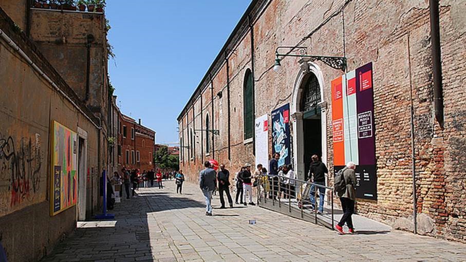 People walking down a brick side street under a blue sky, flanked on the right by a brick building.